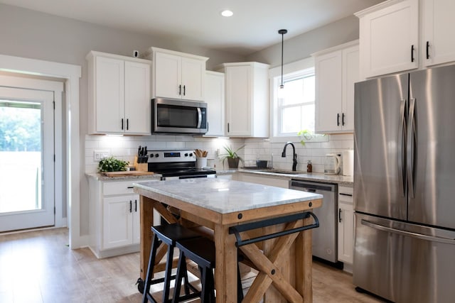 kitchen featuring white cabinets, decorative light fixtures, stainless steel appliances, and light stone counters