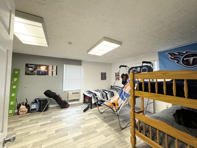 bedroom with a wall unit AC, light hardwood / wood-style flooring, and a textured ceiling