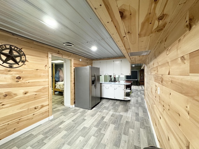 kitchen featuring stainless steel refrigerator with ice dispenser, white cabinetry, wood ceiling, and wood walls