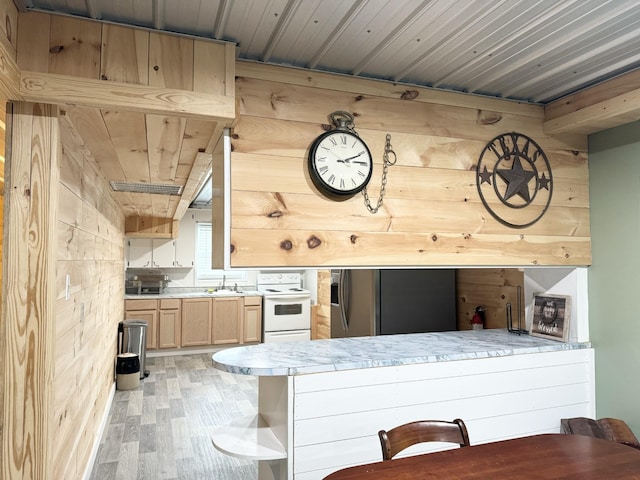 kitchen featuring stainless steel fridge with ice dispenser, electric range, light brown cabinets, and wood walls