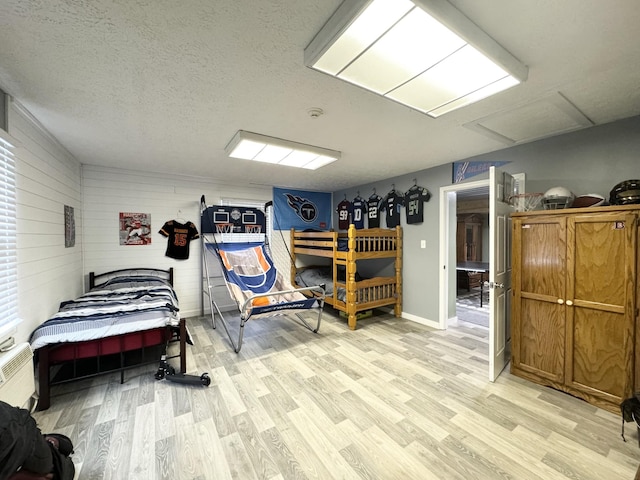 bedroom with wood walls, a textured ceiling, and light wood-type flooring