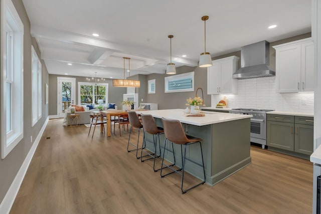 kitchen featuring stainless steel range, wall chimney exhaust hood, beamed ceiling, pendant lighting, and decorative backsplash