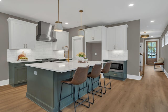 kitchen with white cabinets, decorative light fixtures, wall chimney exhaust hood, and sink