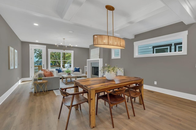 dining space with beam ceiling, a large fireplace, and light hardwood / wood-style floors