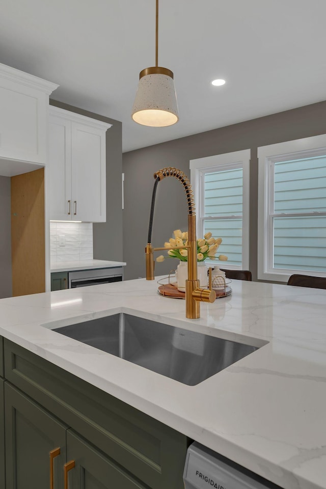 kitchen featuring light stone countertops, hanging light fixtures, green cabinets, and sink