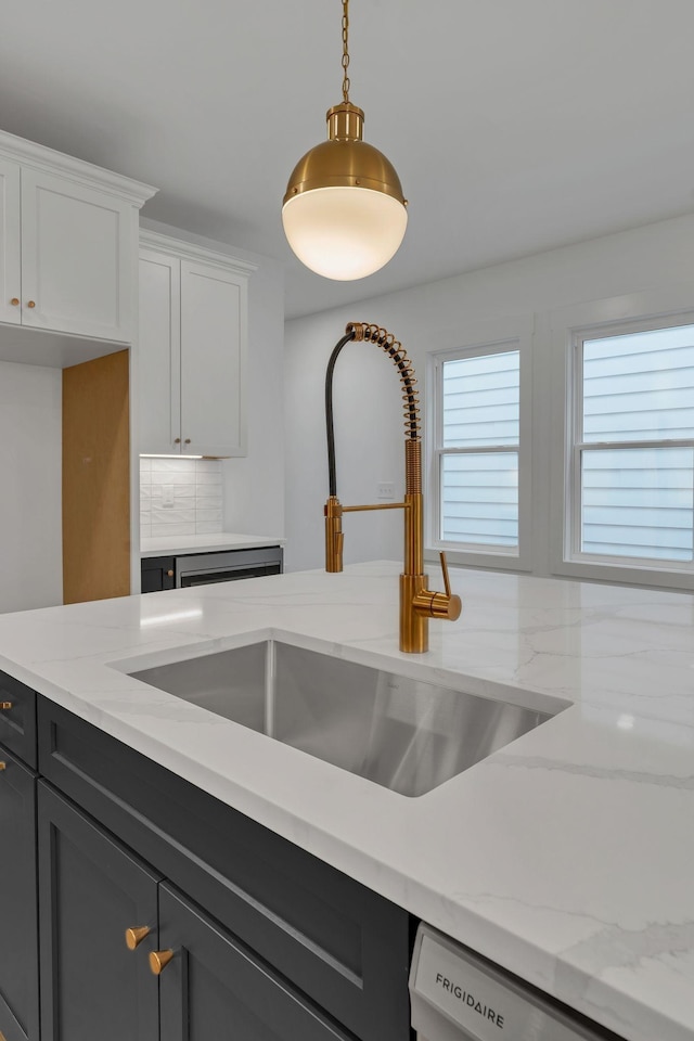 kitchen featuring light stone countertops, dishwasher, sink, decorative light fixtures, and white cabinets