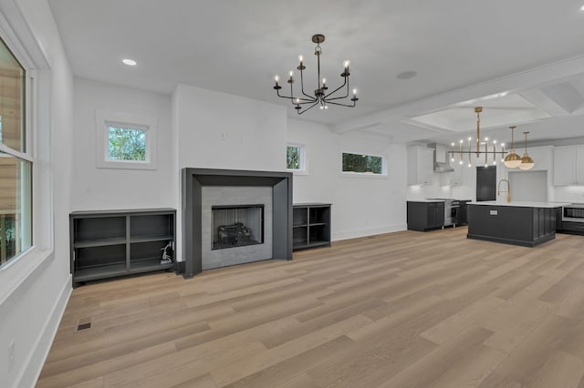 unfurnished living room featuring a notable chandelier, beam ceiling, sink, and light hardwood / wood-style flooring