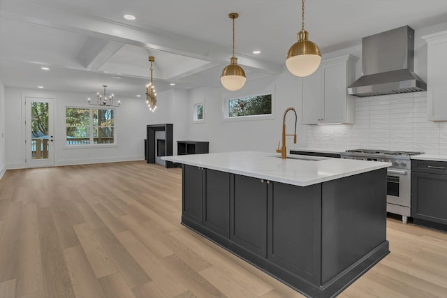 kitchen with high end range, a kitchen island with sink, sink, wall chimney range hood, and hanging light fixtures