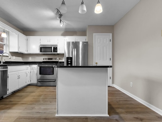 kitchen with sink, stainless steel appliances, decorative light fixtures, white cabinets, and hardwood / wood-style flooring