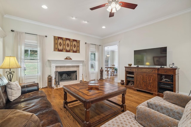 living room featuring a tile fireplace, ornamental molding, ceiling fan, and light hardwood / wood-style floors