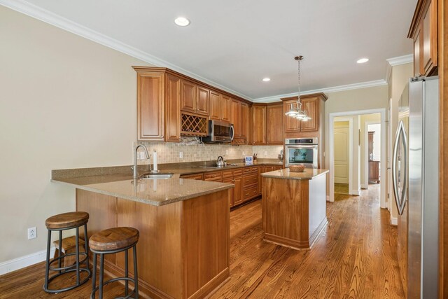 kitchen featuring appliances with stainless steel finishes, stone countertops, sink, hanging light fixtures, and kitchen peninsula