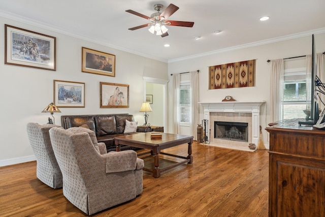 living room featuring ornamental molding, wood-type flooring, ceiling fan, and a fireplace