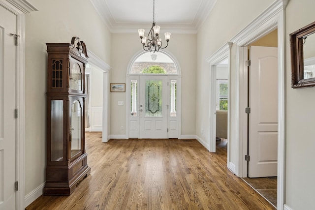 foyer entrance featuring hardwood / wood-style flooring, ornamental molding, and a notable chandelier