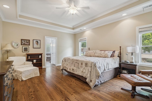 bedroom featuring ceiling fan, hardwood / wood-style floors, ensuite bathroom, a tray ceiling, and ornamental molding