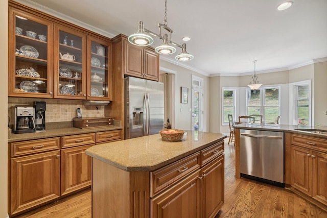 kitchen with crown molding, stainless steel appliances, a center island, decorative light fixtures, and light wood-type flooring