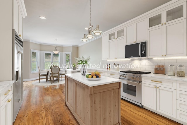 kitchen with high end appliances, white cabinetry, decorative light fixtures, and a kitchen island