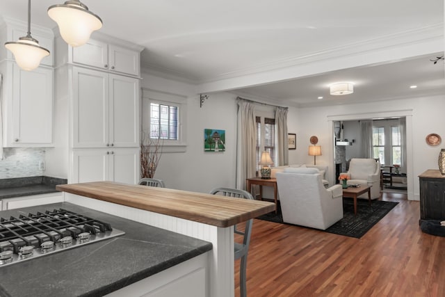 kitchen featuring white cabinetry, dark wood-type flooring, pendant lighting, stainless steel gas stovetop, and a breakfast bar area