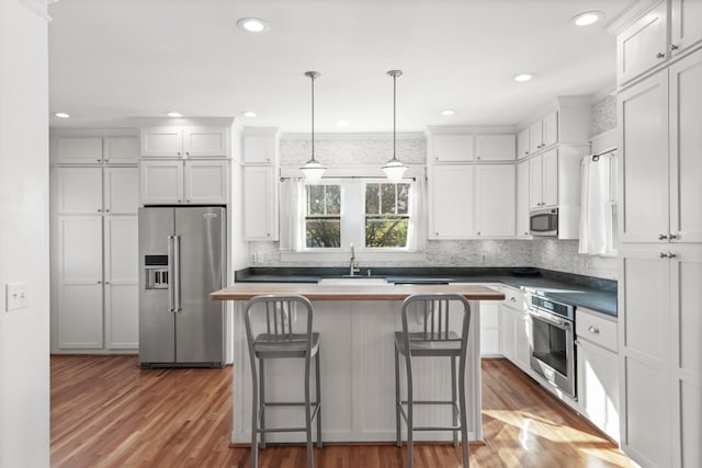 kitchen featuring white cabinets, a kitchen bar, hanging light fixtures, and appliances with stainless steel finishes