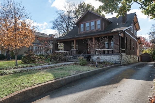 view of front of house with covered porch, a garage, an outdoor structure, and a front yard