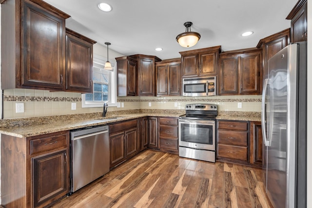 kitchen featuring appliances with stainless steel finishes, decorative light fixtures, dark hardwood / wood-style flooring, light stone counters, and sink