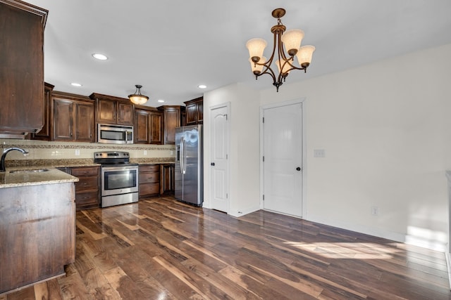 kitchen featuring stainless steel appliances, hanging light fixtures, a chandelier, light stone counters, and sink