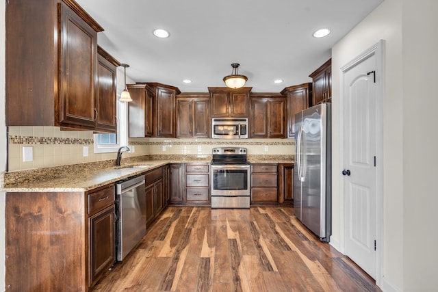 kitchen featuring appliances with stainless steel finishes, dark hardwood / wood-style floors, pendant lighting, light stone counters, and sink