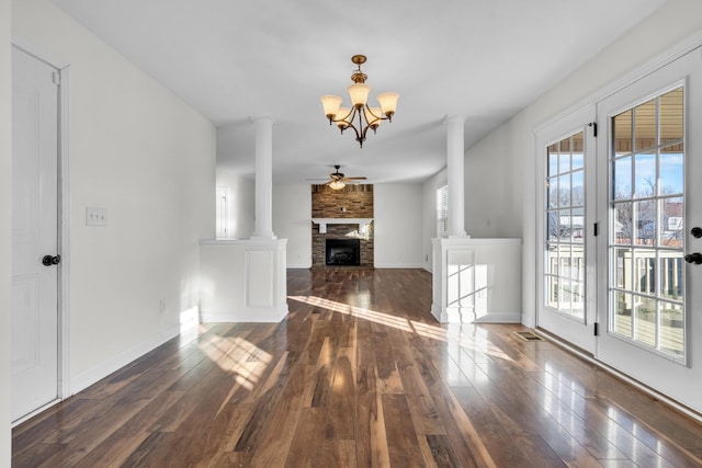 unfurnished living room with dark wood-type flooring, a fireplace, a wealth of natural light, and ceiling fan with notable chandelier