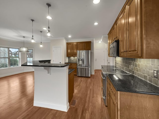 kitchen featuring hanging light fixtures, decorative backsplash, stainless steel appliances, and a kitchen island with sink