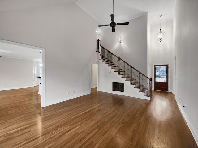 unfurnished living room featuring ceiling fan with notable chandelier, a towering ceiling, crown molding, and dark wood-type flooring