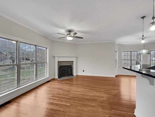 unfurnished living room featuring plenty of natural light, wood-type flooring, ornamental molding, and a tiled fireplace