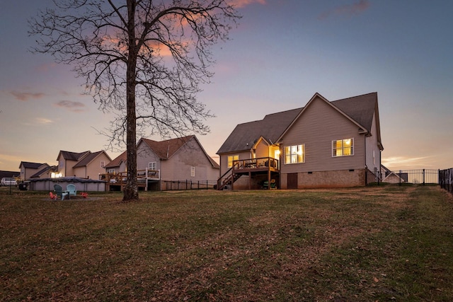 back house at dusk featuring a wooden deck and a lawn