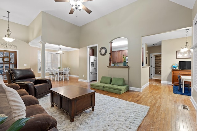 living room featuring ornate columns, high vaulted ceiling, light hardwood / wood-style floors, and ceiling fan with notable chandelier