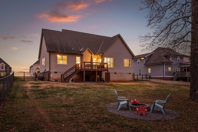 back house at dusk featuring a lawn, a deck, and an outdoor fire pit