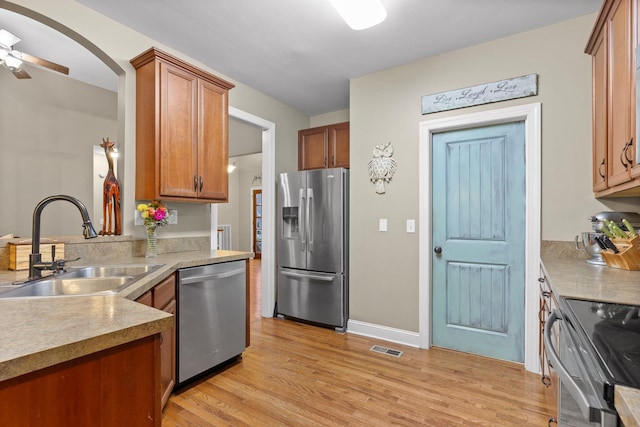 kitchen with appliances with stainless steel finishes, light wood-type flooring, ceiling fan, and sink