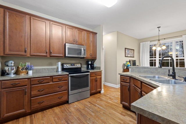 kitchen featuring appliances with stainless steel finishes, sink, pendant lighting, light hardwood / wood-style flooring, and an inviting chandelier