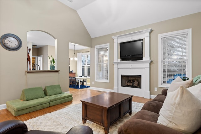 living room with a notable chandelier, a large fireplace, lofted ceiling, and light hardwood / wood-style flooring