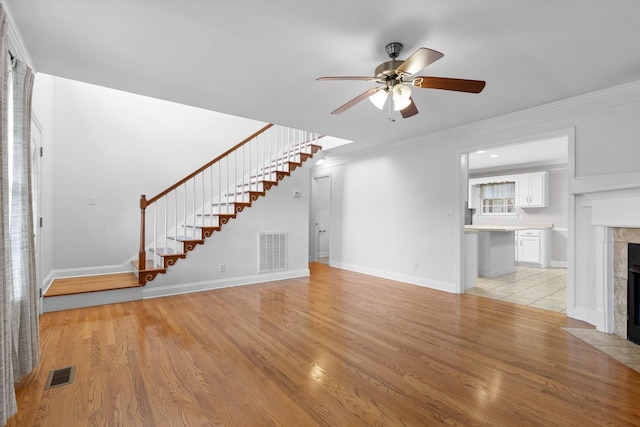 unfurnished living room with ceiling fan, crown molding, a tile fireplace, and light hardwood / wood-style flooring