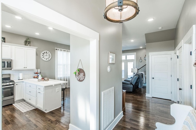 kitchen featuring tasteful backsplash, dark hardwood / wood-style flooring, kitchen peninsula, white cabinets, and appliances with stainless steel finishes