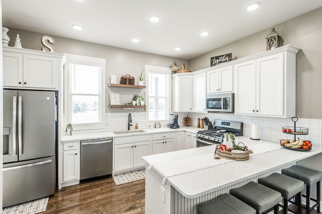 kitchen with kitchen peninsula, appliances with stainless steel finishes, sink, white cabinets, and a breakfast bar area