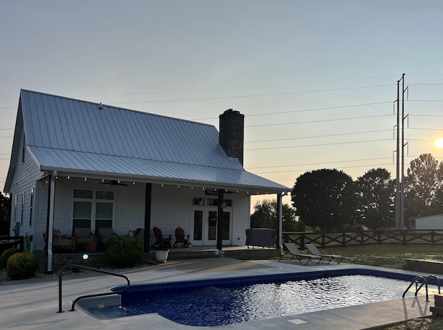 pool at dusk with ceiling fan, a patio area, and french doors