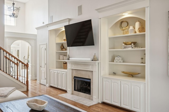 living room featuring a fireplace, built in shelves, a chandelier, and light hardwood / wood-style flooring