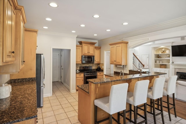 kitchen with kitchen peninsula, dark stone counters, ornamental molding, black gas range oven, and stainless steel refrigerator