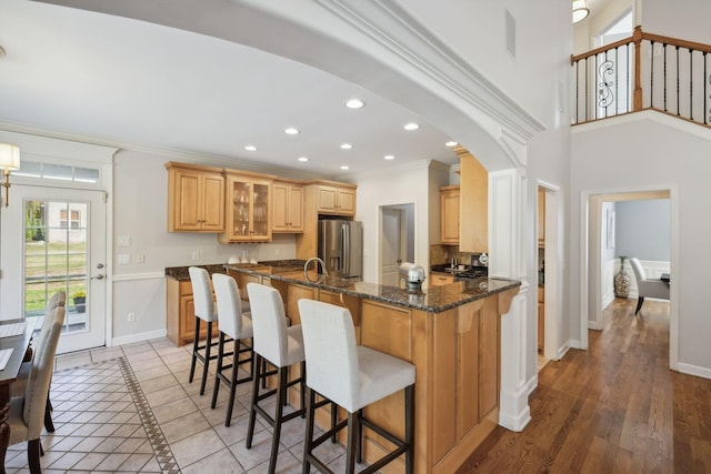 kitchen featuring kitchen peninsula, stainless steel fridge, dark stone counters, a breakfast bar, and ornamental molding