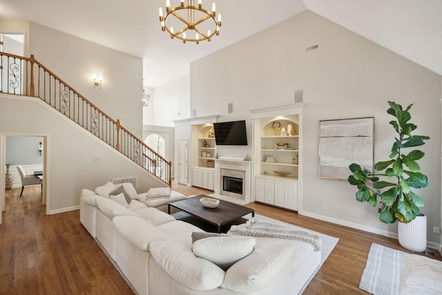 living room featuring built in features, dark wood-type flooring, high vaulted ceiling, and an inviting chandelier