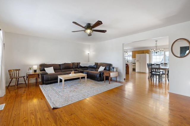 living room featuring ceiling fan with notable chandelier and light wood-type flooring