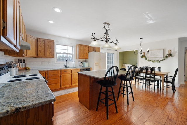 kitchen featuring hanging light fixtures, a center island, white fridge with ice dispenser, range with electric cooktop, and sink