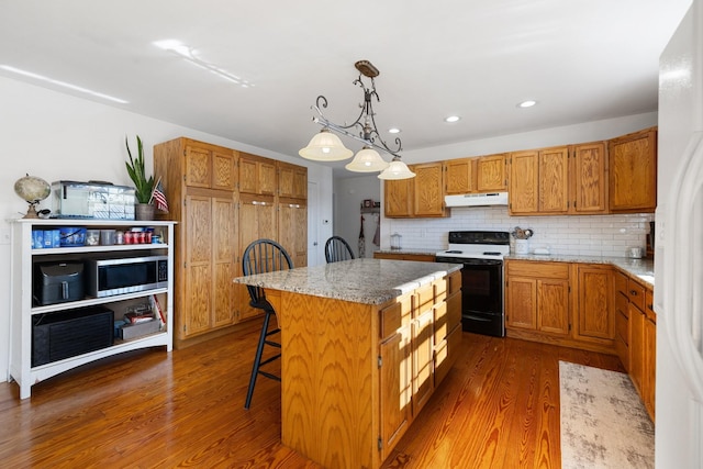 kitchen with hanging light fixtures, a center island, decorative backsplash, electric range, and a breakfast bar area