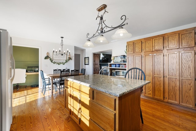 kitchen with wood-type flooring, hanging light fixtures, a center island, white refrigerator, and light stone counters