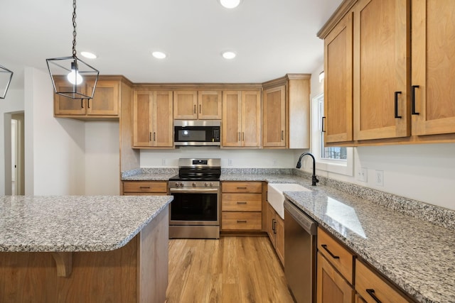 kitchen with sink, light wood-type flooring, decorative light fixtures, light stone counters, and stainless steel appliances