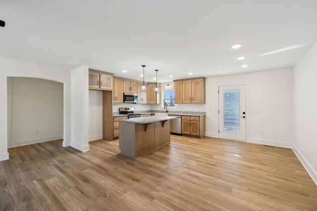 kitchen with light wood-type flooring, light stone counters, stainless steel appliances, a kitchen island, and hanging light fixtures